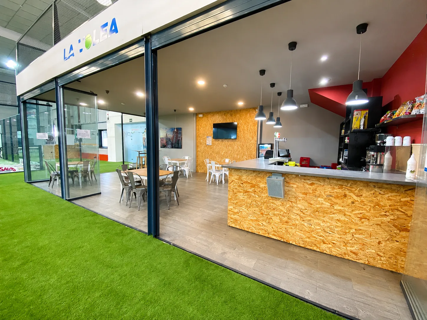 Cafetería del club con barra de madera, mesas y televisión
